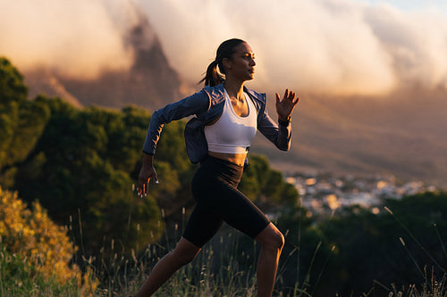 Slim female runner exercising against stunning sunset. Woman in sportswear running at sunset outdoors.