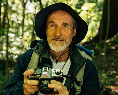 Close-up portrait of senior tourist with a film camera in a forest. Mature male with a retro camera during his hike.