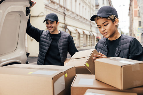 Two delivery people working at van trunk. Woman checking informa