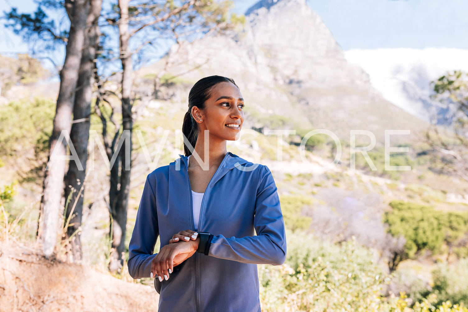 Smiling slim woman with smartwatches relaxing after training outdoors. Young female looking away during morning walk.