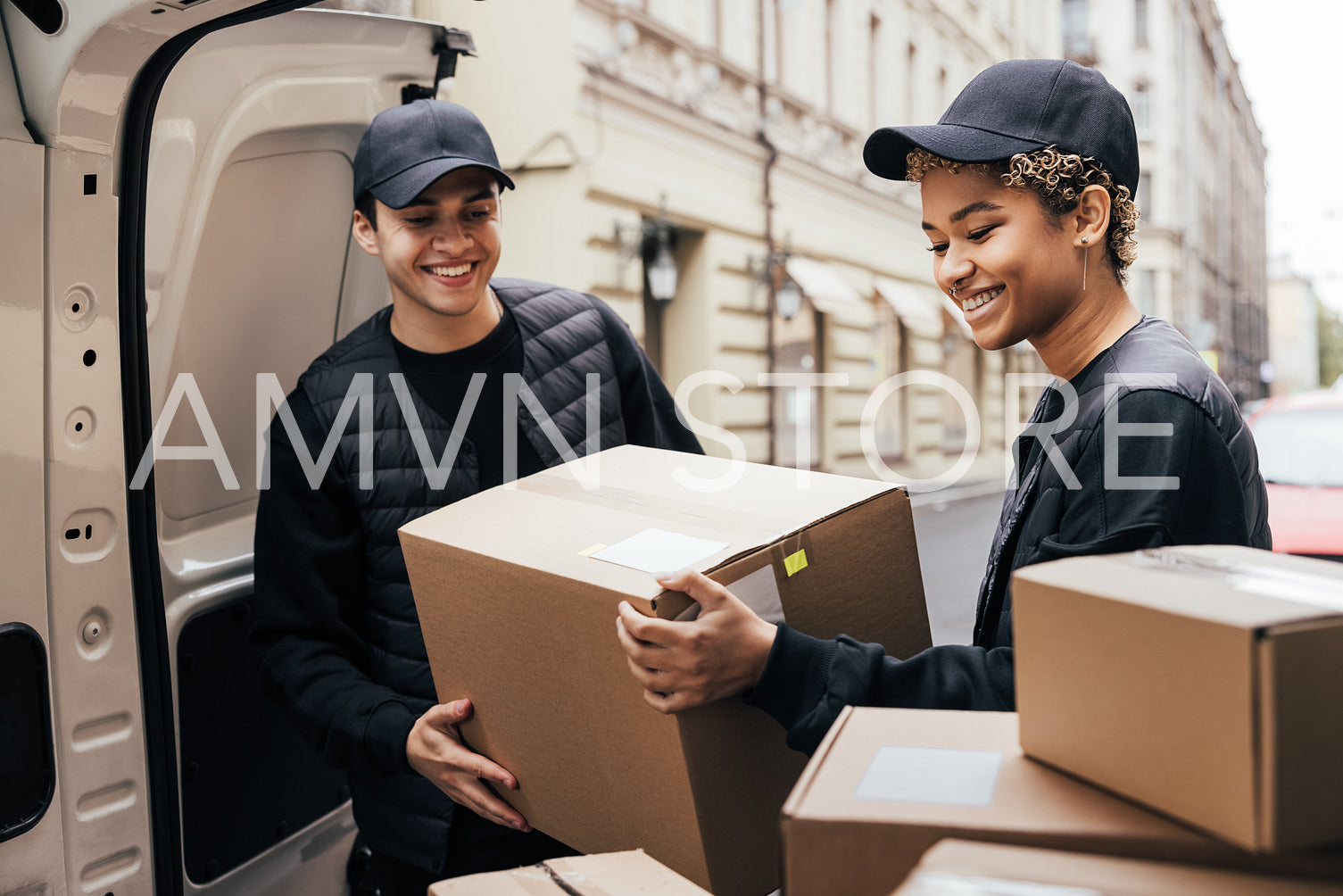 Two smiling couriers unloading cardboard boxes from van in the c