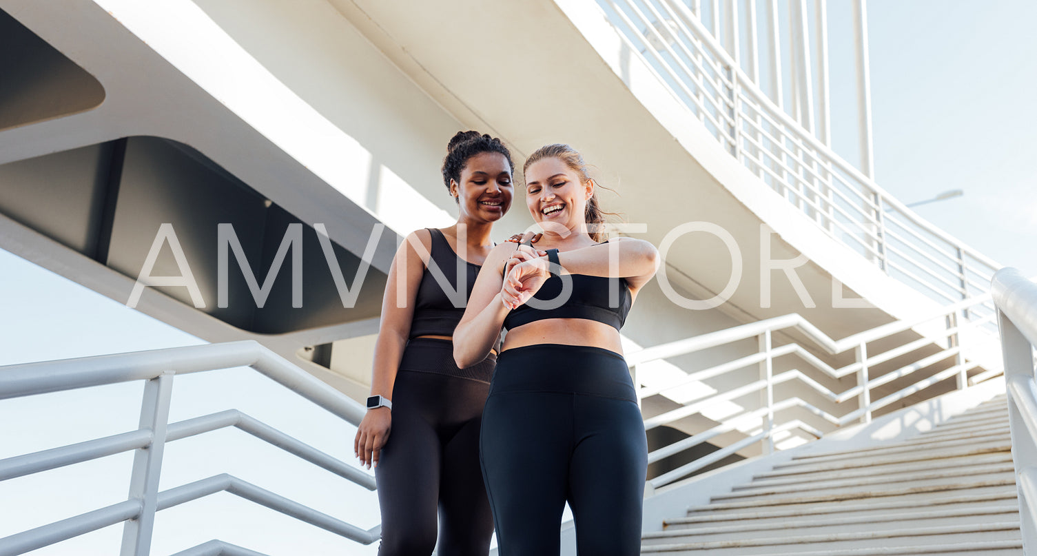 Happy plus-size woman showing her friend workout results on smartwatches. Two friends in sportswear looking at smartwatches.