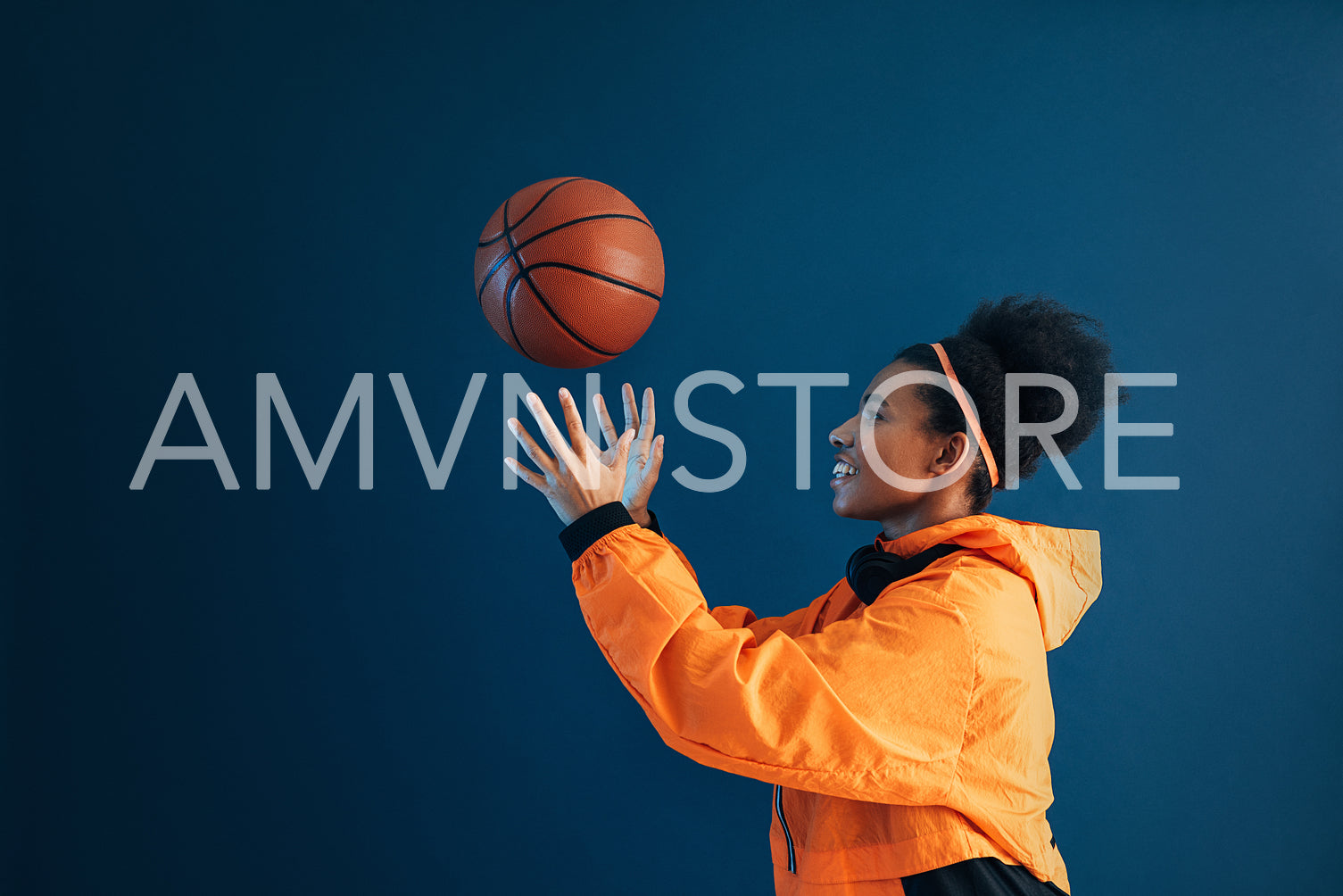 Side view of smiling woman in orange fitness attire catching basketball over blue backdrop