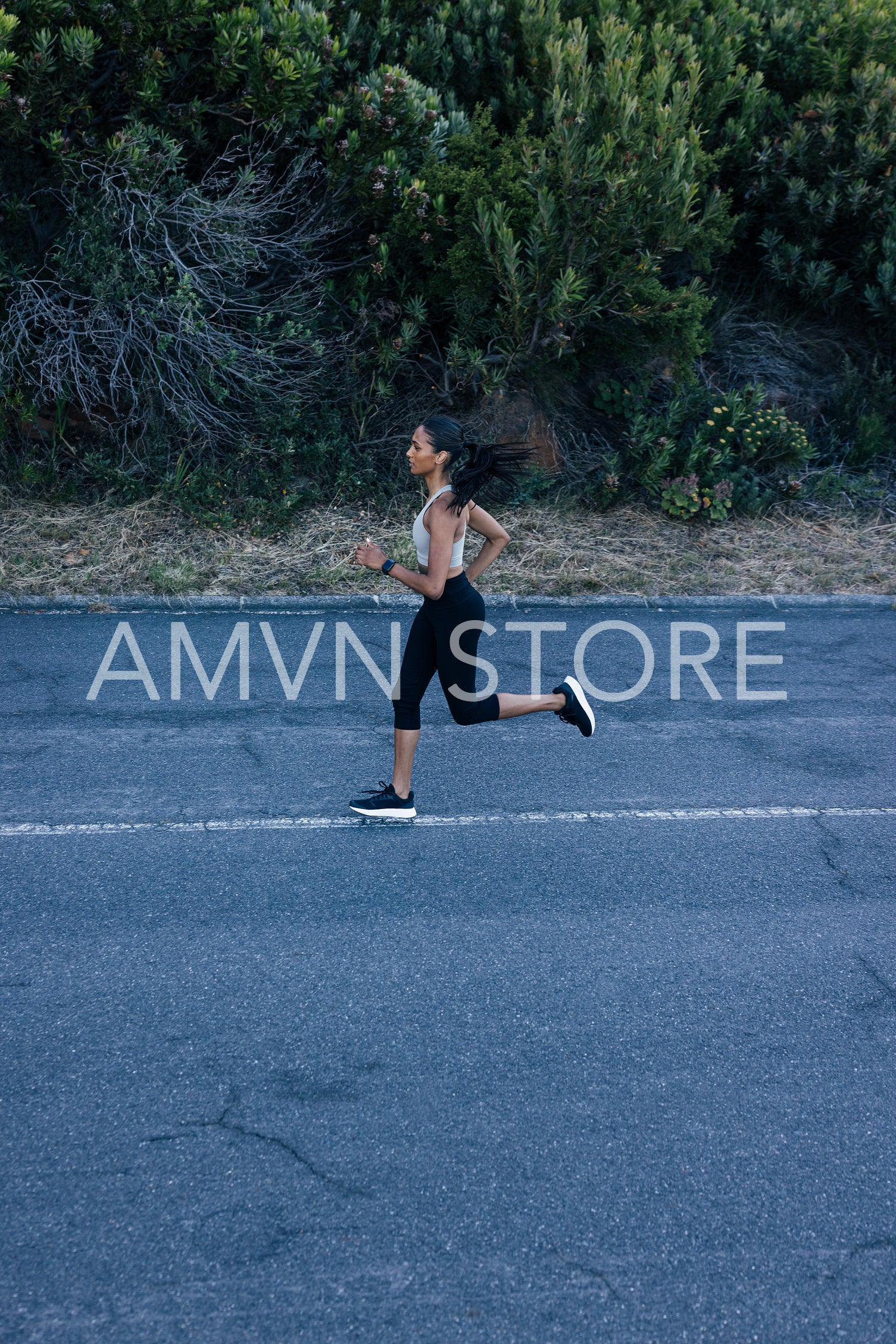 Side view of full length of slim female running on an abandoned road in a natural park. Woman practicing running outdoors. 