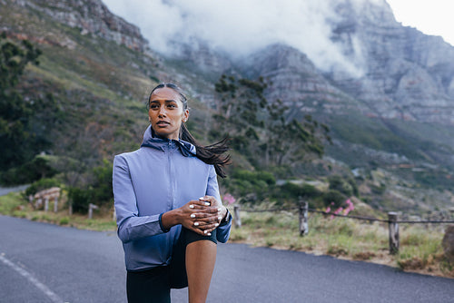 Young woman athlete warming up before workout in natural park. Confident sportswoman flexing leg outdoors.