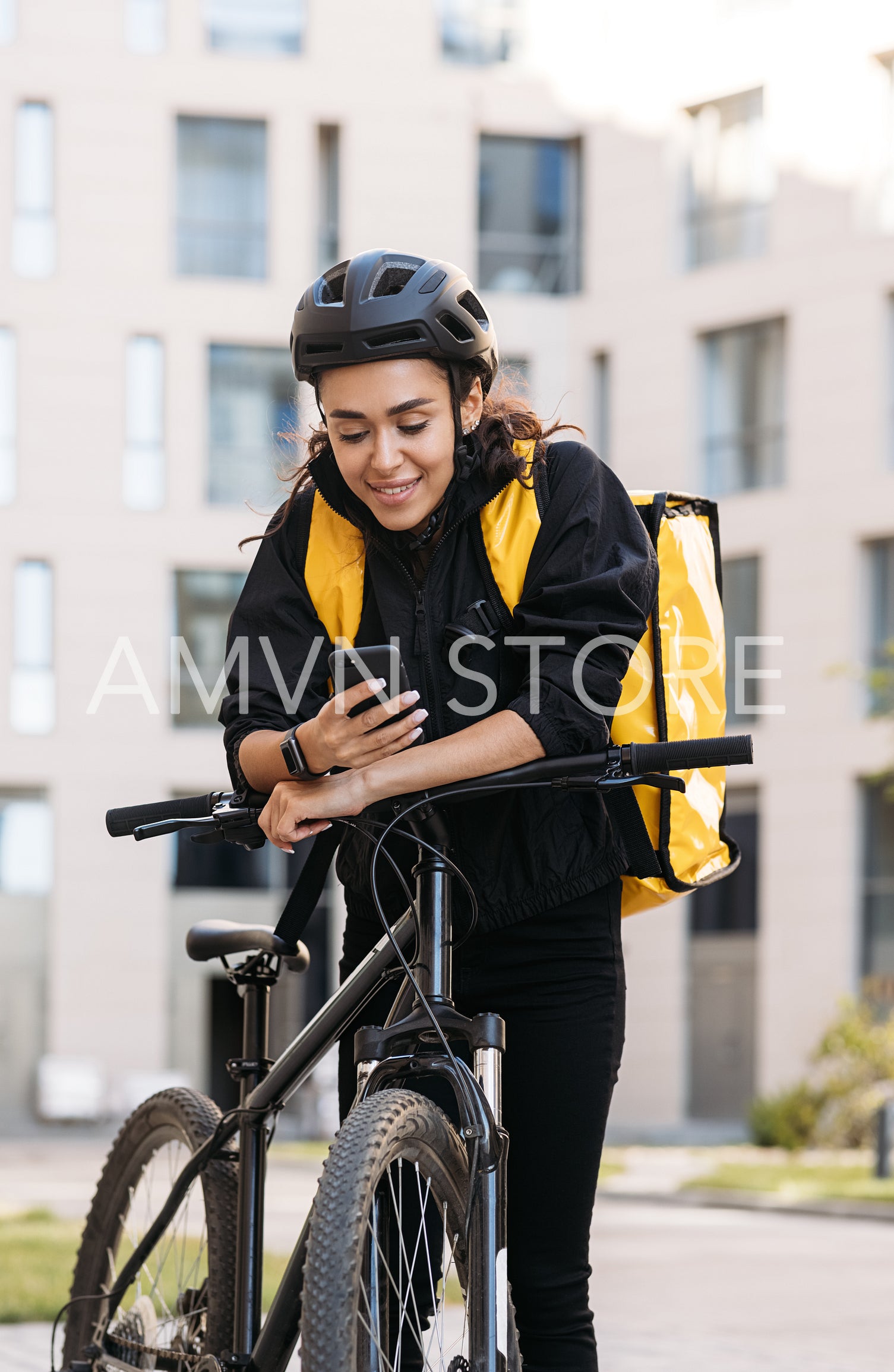 Smiling woman messenger with bicycle and thermal backpack holding a smartphone in the city