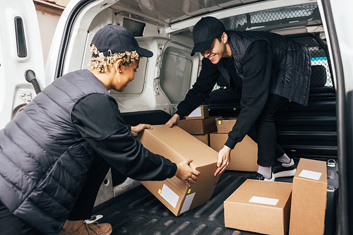 Two people working for delivery company unloading cardboard boxes from van