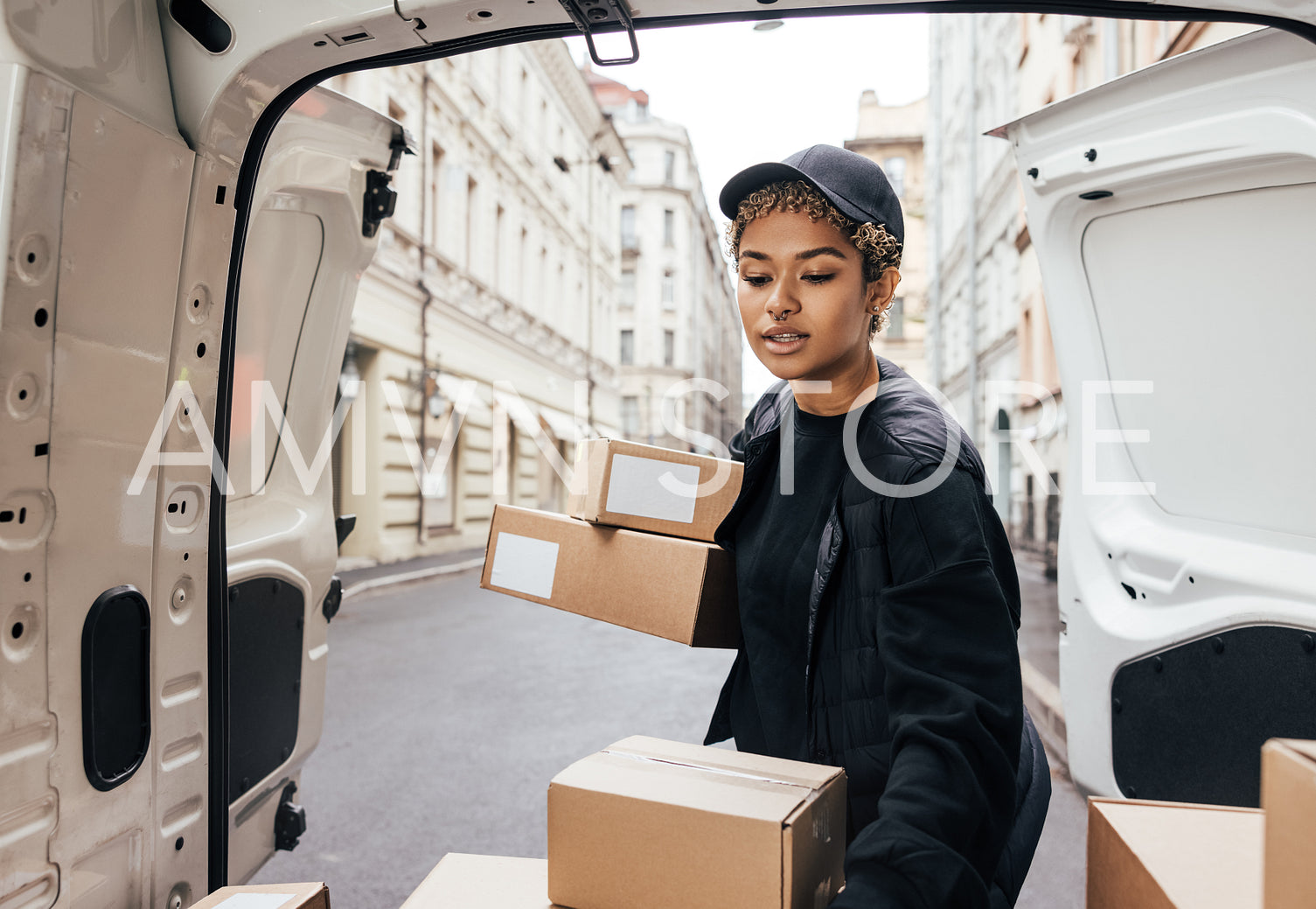 Woman courier in uniform carefully unloading cardboard boxes fro