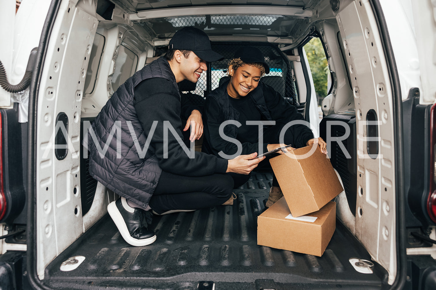 Two smiling couriers sitting in delivery van checking informatio