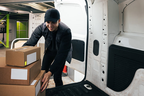 Smiling male courier working in warehouse upload boxes into a va