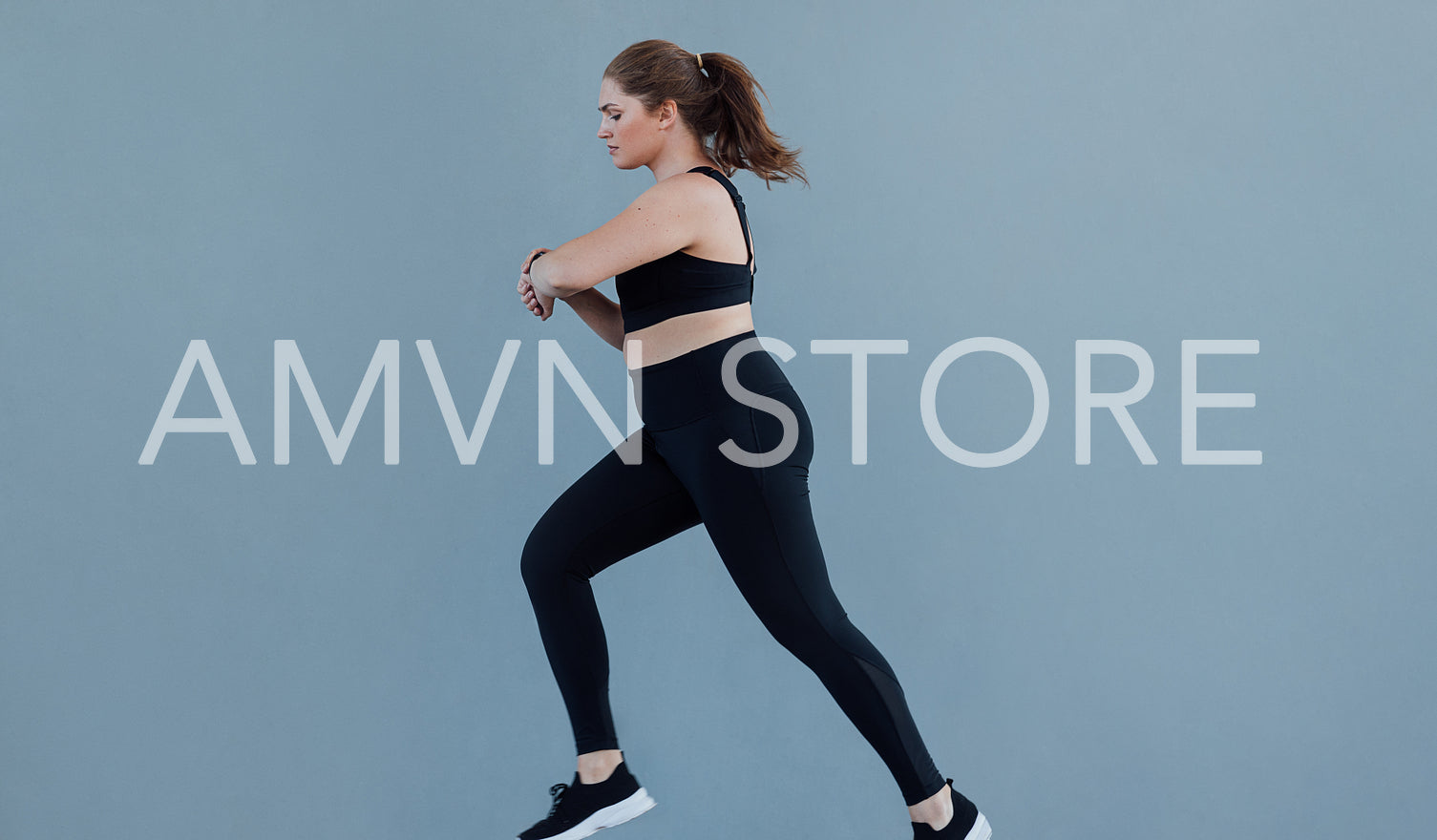 Side view of plus size female running against a grey wall wearing black fitness attire. Young woman with plus size body type jogging and looking at her smartwatch.