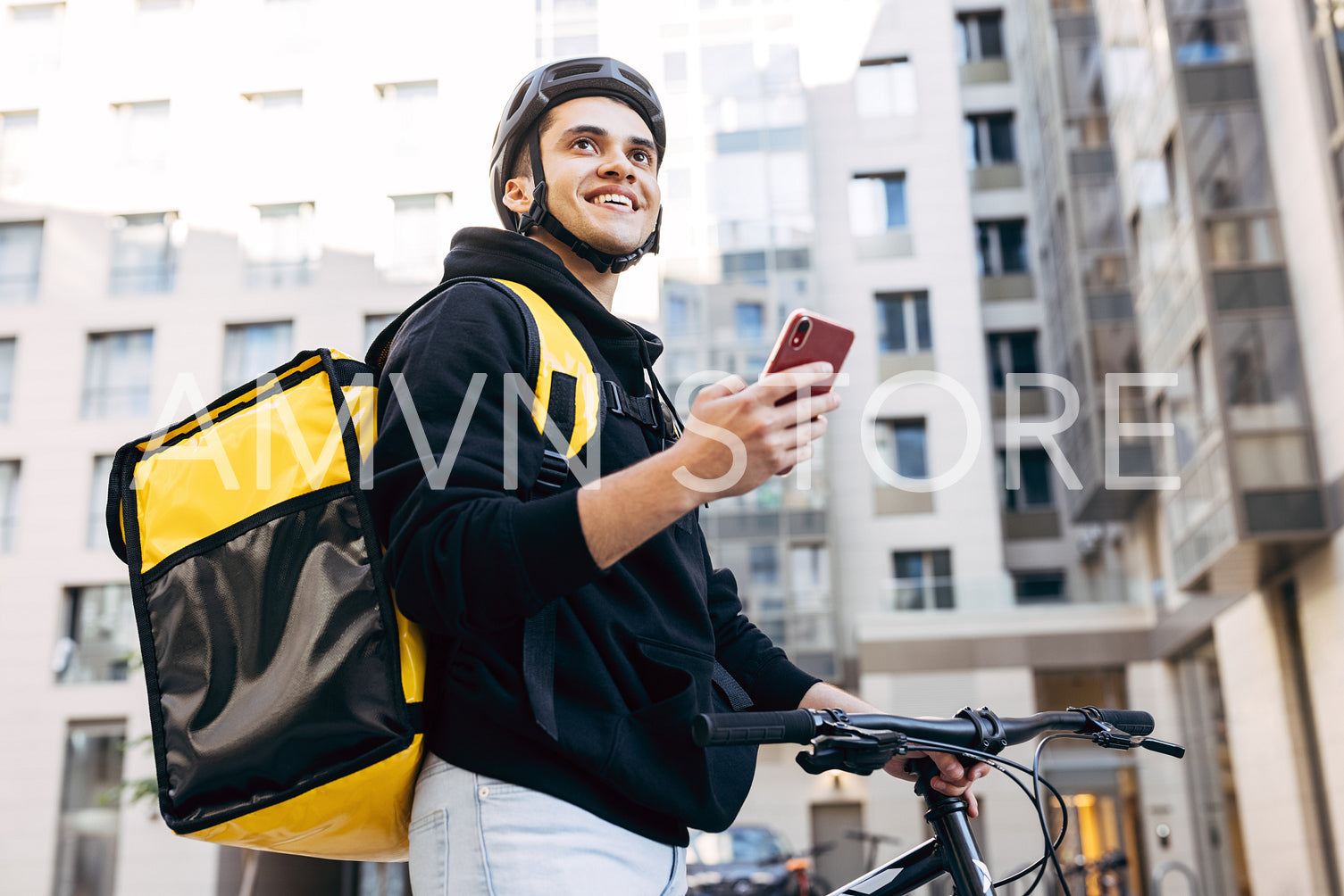 Portrait of delivery man holding a mobile phone, wearing thermal backpack standing against apartment building