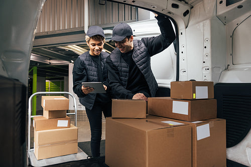 Two couriers in uniform standing at car trunk in warehouse check