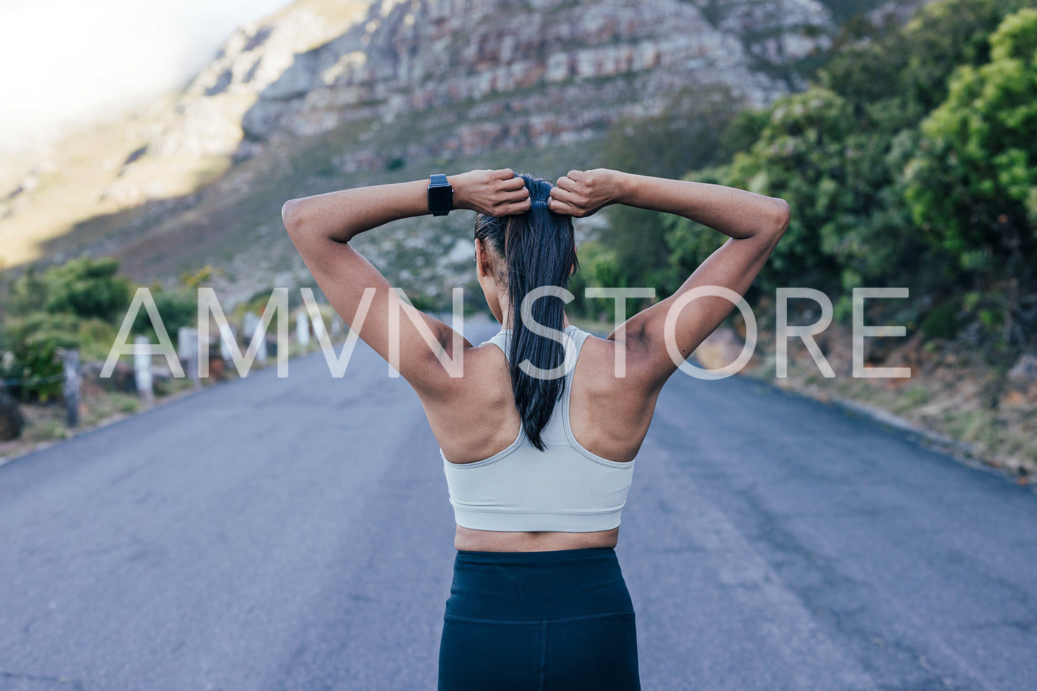 Back view of a young slim sportswoman adjusting her hair while standing outdoors in the middle of the abandoned road 