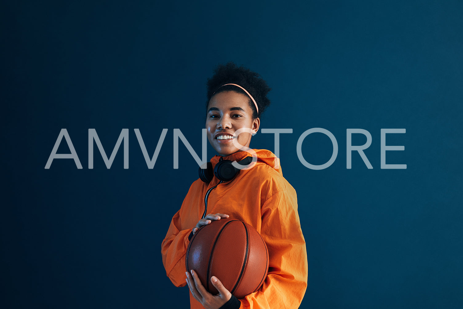 Smiling female with basketball wearing orange sportswear and looking at camera. Professional basketball player posing in studio.