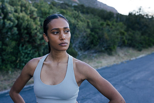 Young and confident woman athlete standing on abandoned road and looking away, taking a break during outdoor workout