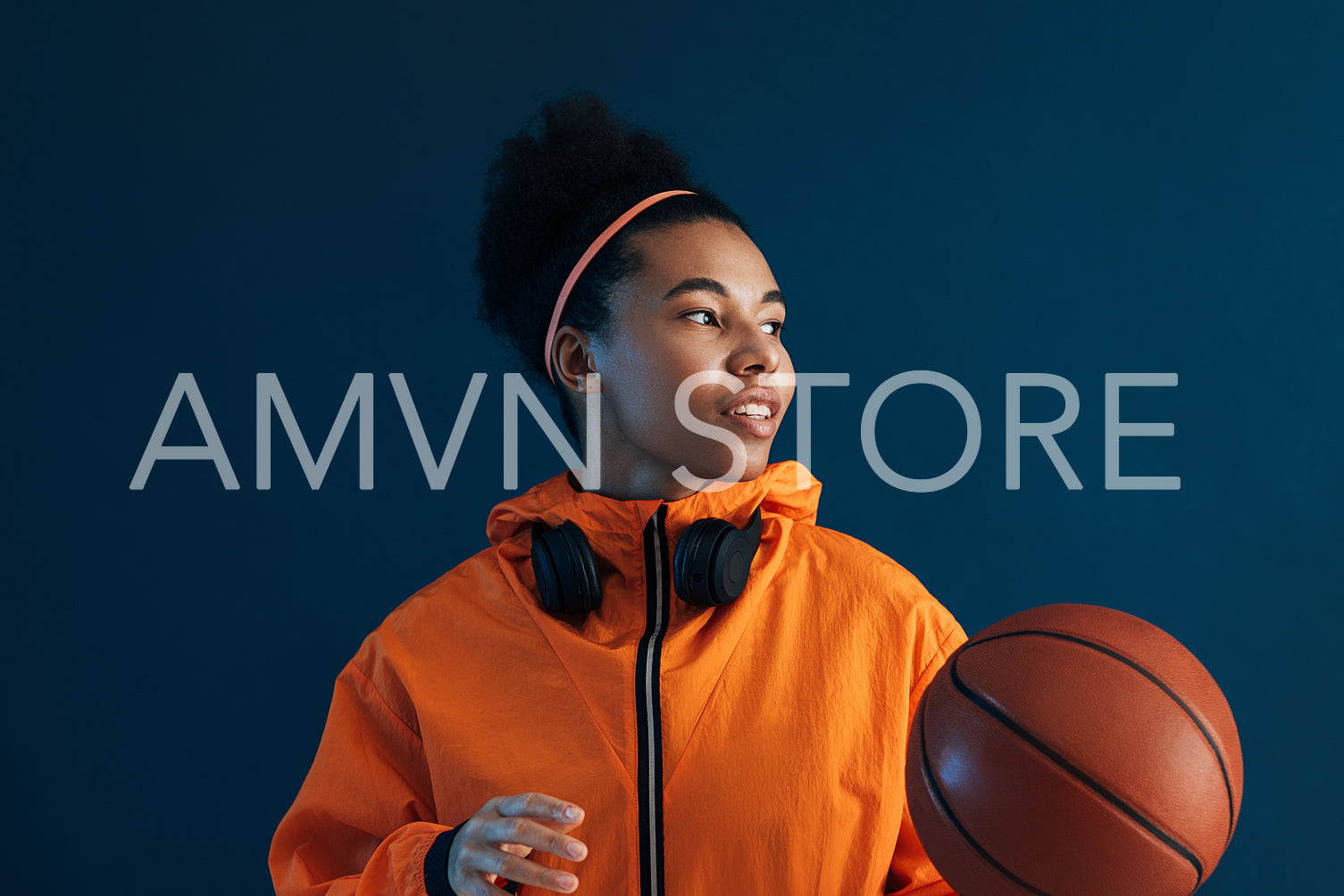 Portrait of a female professional basketball player looking away in a studio. Confident female basketball player wearing orange sportswear.