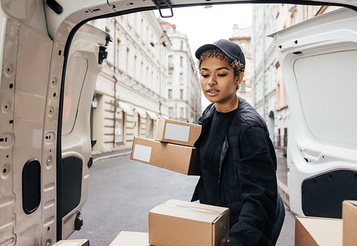 Woman courier in uniform carefully unloading cardboard boxes fro