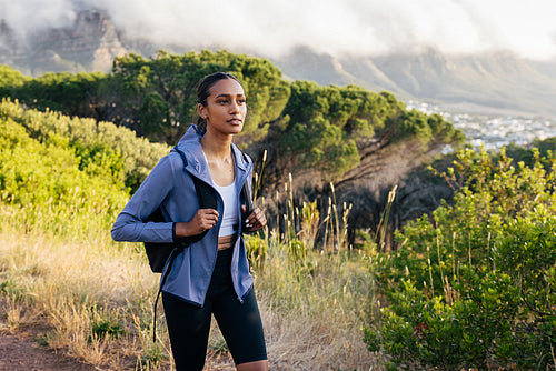 Woman with backpack and sportswear walking at sunset. Young female wearing fitness attire hiking in natural park.