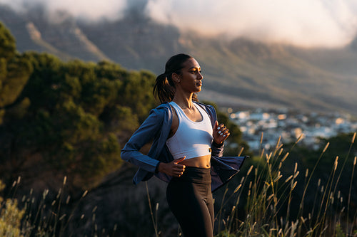 Confident female runner practicing outdoors at stunning sunset. Side view of slim woman in fitness attire jogging at sunset.