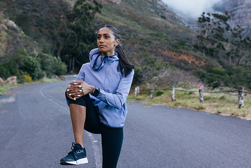 Slim confident female in fitness attire warming up her lower body on an abandoned road