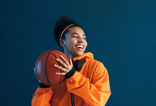 Happy professional basketball player holding basketball over blue backdrop in the studio and looking away