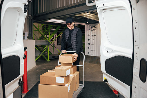 Smiling courier in uniform checking cardboard boxes on a cart wh