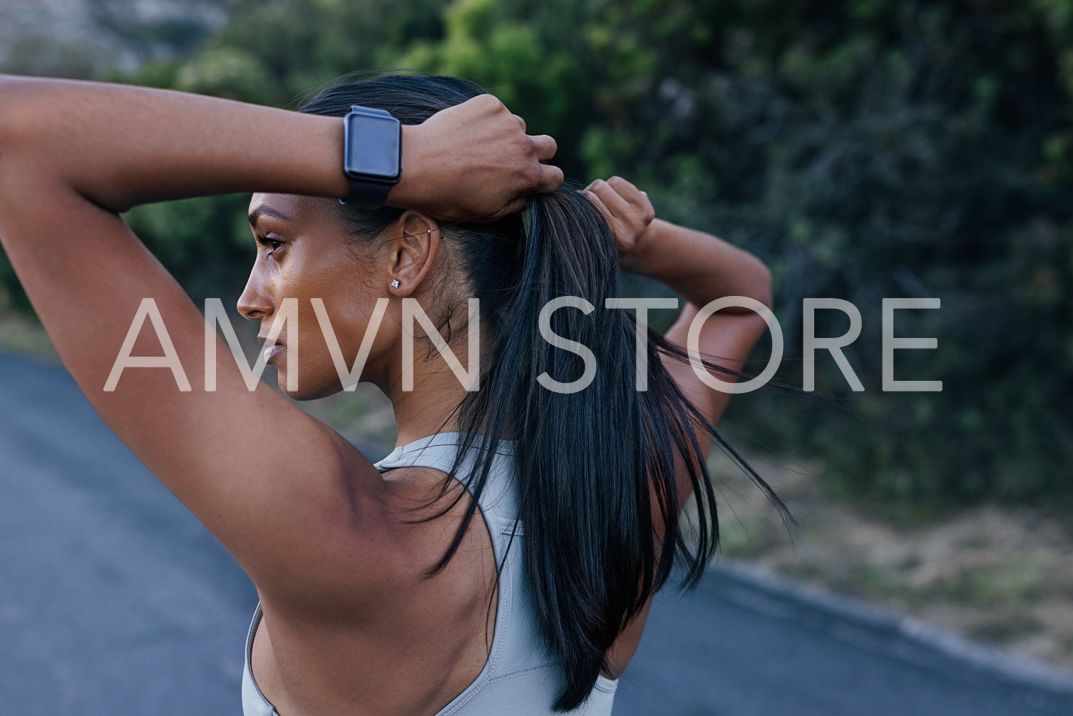 Young sportswoman with smartwatches on her hand adjusting hair during exercises outdoors. Close-up of a female in sportswear taking a break.