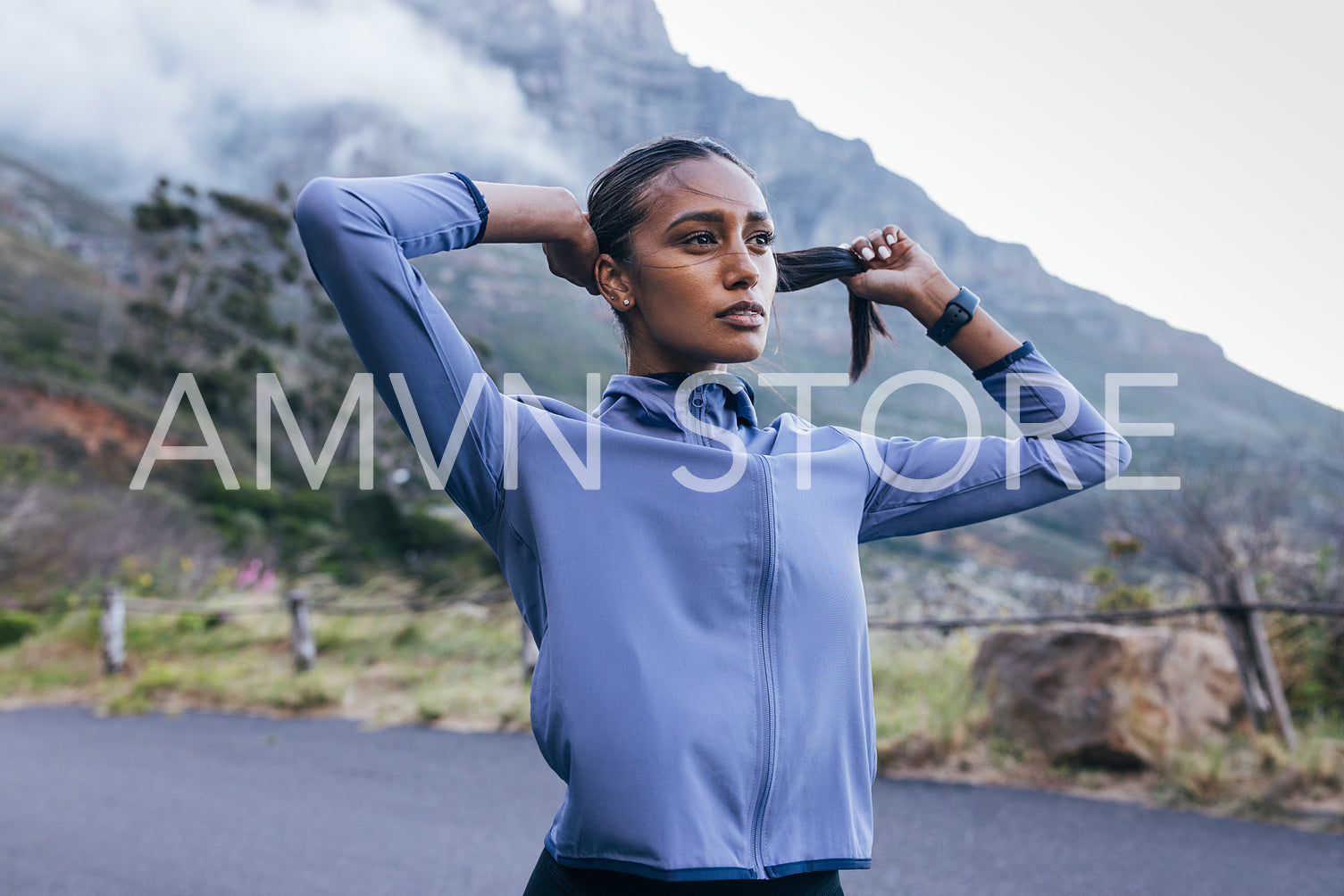 Young slim female in sportswear taking a break to adjust her hair during a run in a natural park