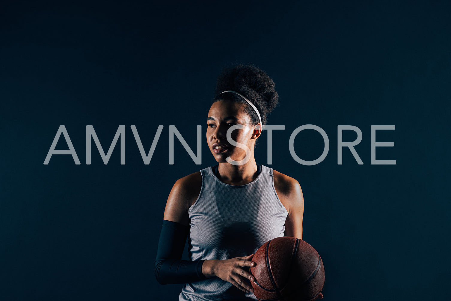 Female basketball player in sportswear over black backdrop. Young professional basketball player with ball, wearing team attire.