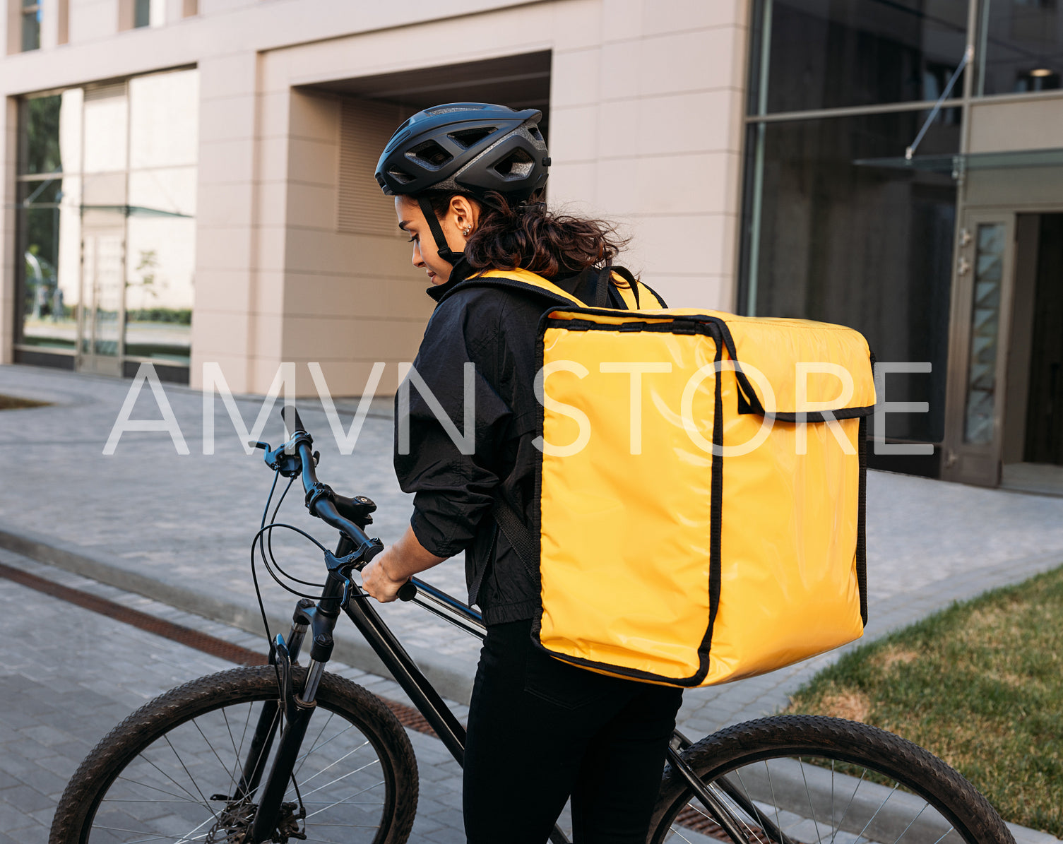 Back view of a female courier standing on a street with a bicycle. Rear view of a woman working on delivery service wearing a helmet and yellow backpack.