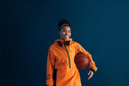 Young woman in orange fitness clothes with a basketball over a blue background