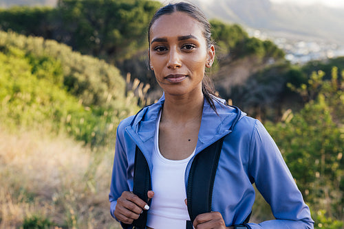 activity, athlete, backpack, beautiful, break, confident, exploration, female, hiking, hill, lifestyle, looking at camera, natural park, one, outdoors, people, person, portrait, real, smiling, sportswoman, standing, sunset, trail run, woman, young