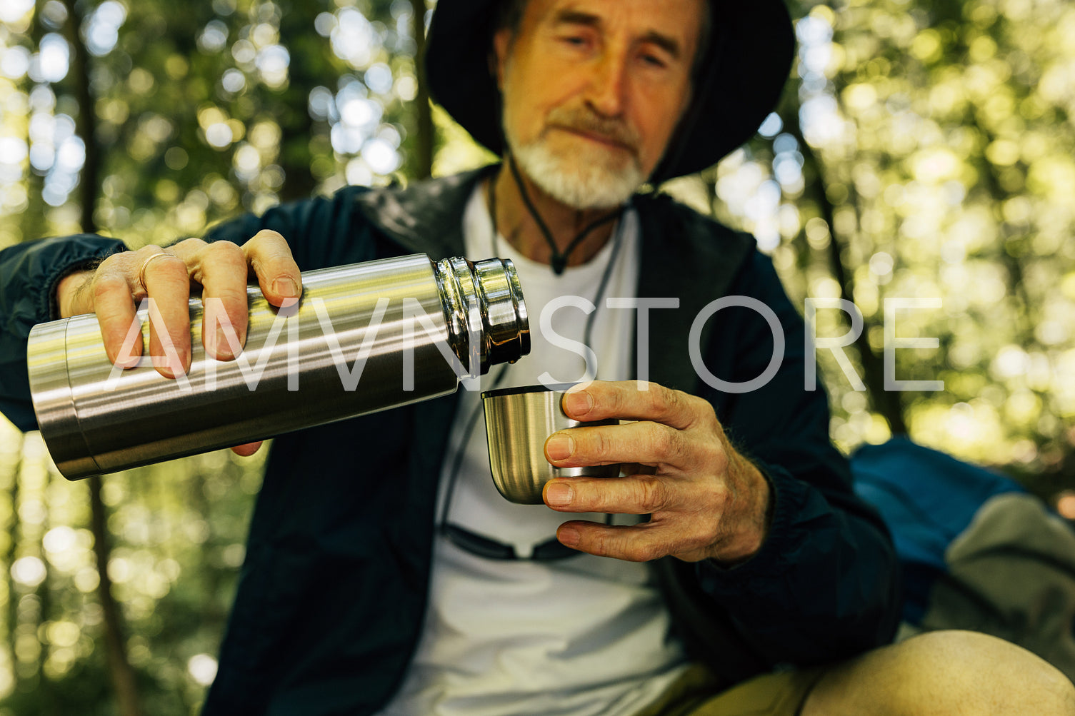 Senior male tourist pouring coffee from a thermos into a cup. Mature tourist with thermos in a forest.