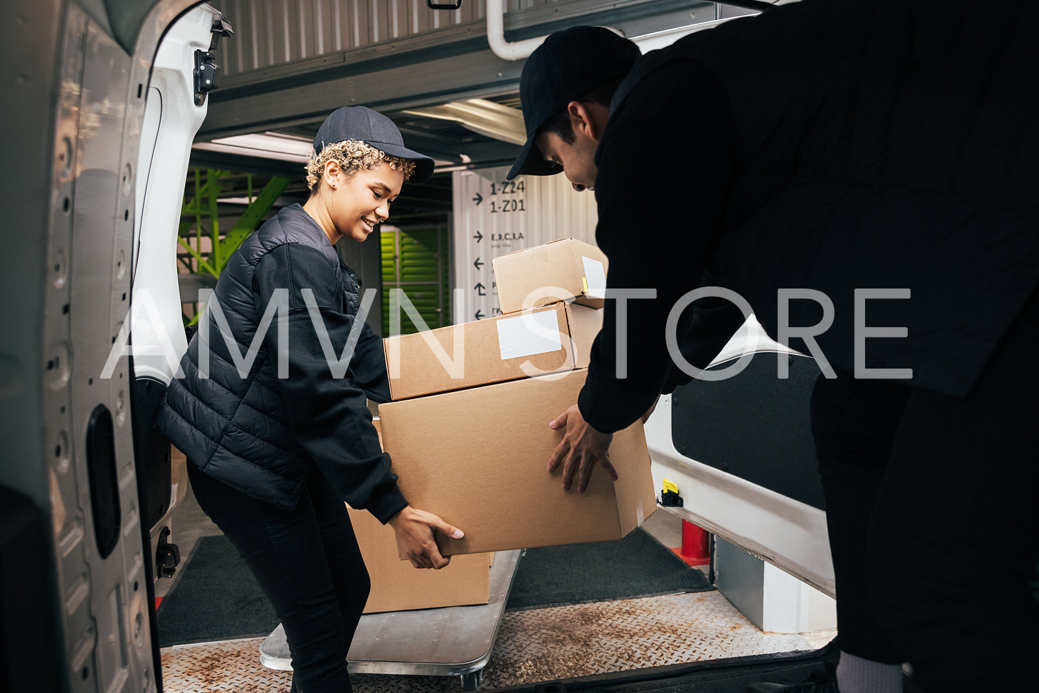 Two couriers stack cardboard boxes in a delivery van. Coworkers