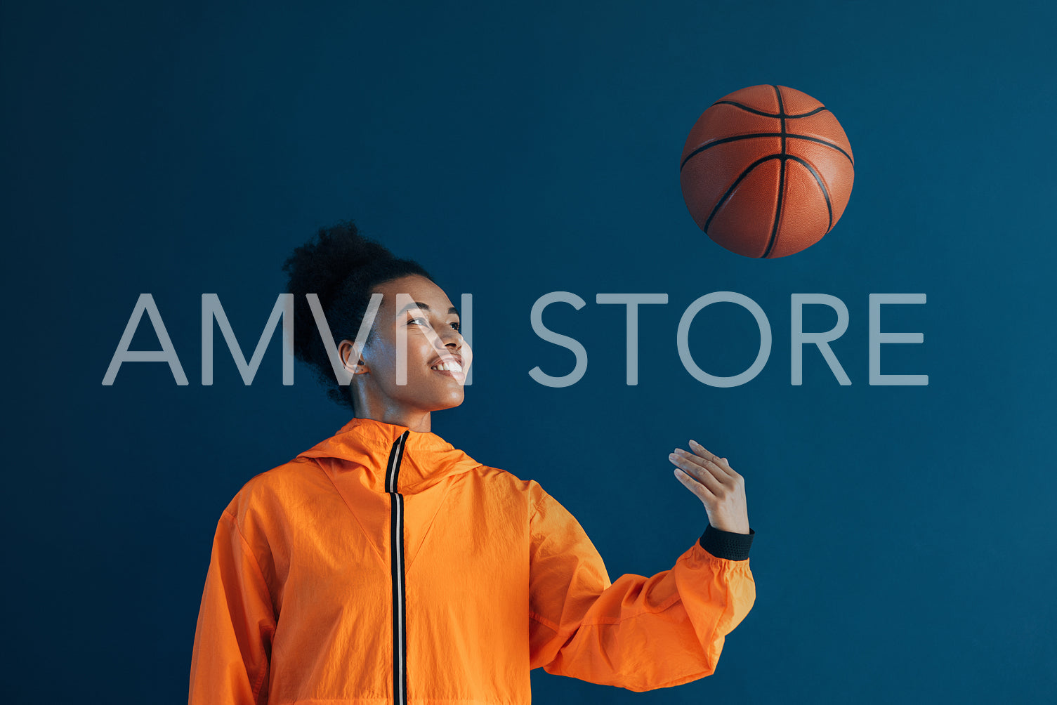 Female basketball player tossing a basketball over a blue background. Young woman in orange sportswear tossing basketball up in studio.