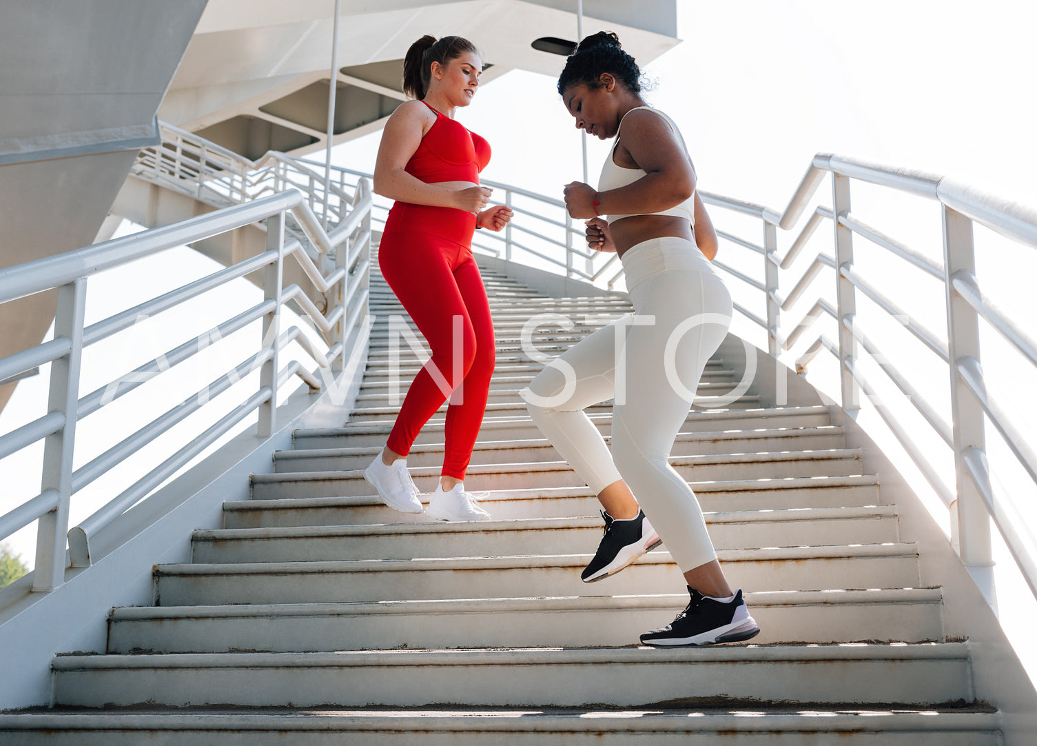 Two female friends running down on stairs. Women with different body types exercise outdoors together.