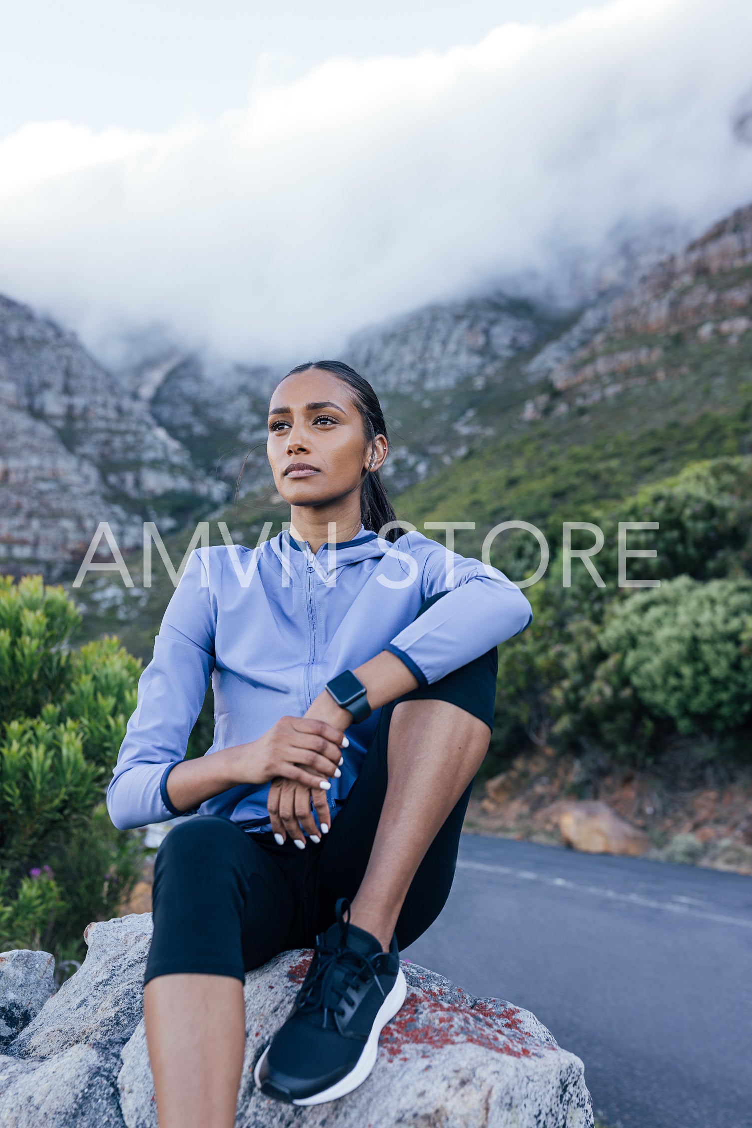 Young sportswoman sitting in the natural park relaxing during workout. Slim female enjoying the view during a trail run.