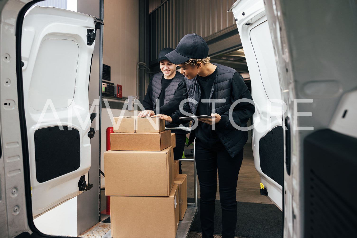 Male courier pushing a cart in a warehouse while coworker checki