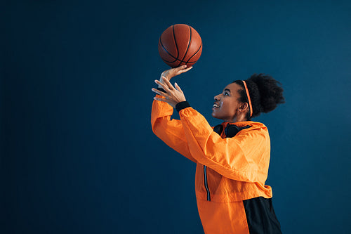 Side view of smiling basketball player in orange fitness attire practicing throwing over blue background