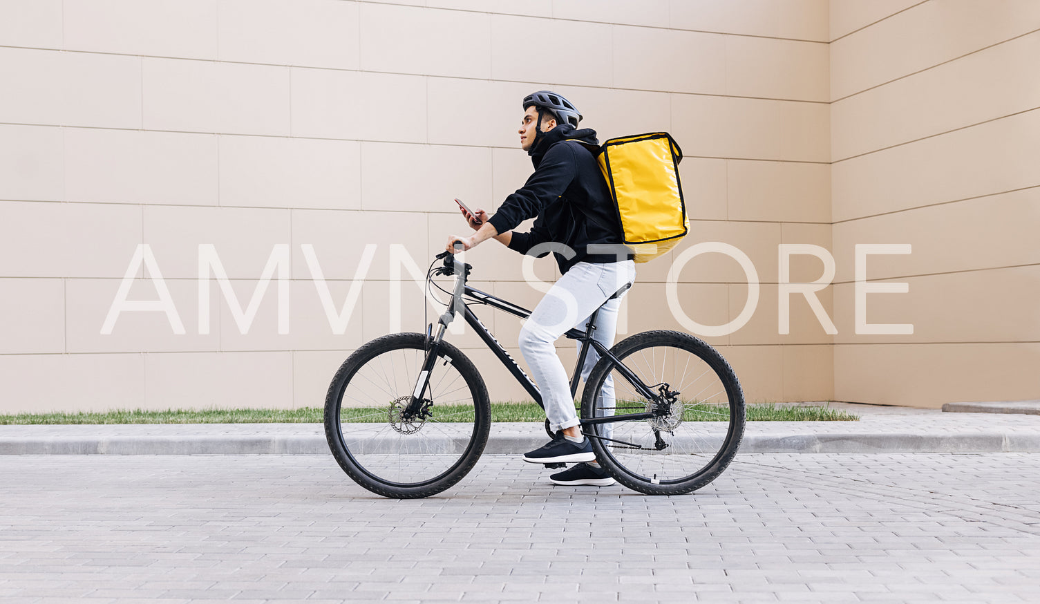 Side view of a young messenger with termal backpack man riding his bike and using mobile phone in the city