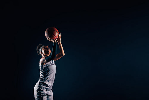 Professional female basketball player throwing basketball against black backdrop. Woman basketball player is ready to throw a ball.