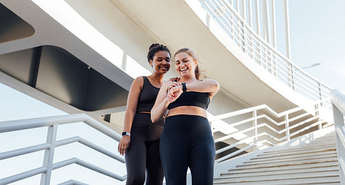 Happy plus-size woman showing her friend workout results on smartwatches. Two friends in sportswear looking at smartwatches.