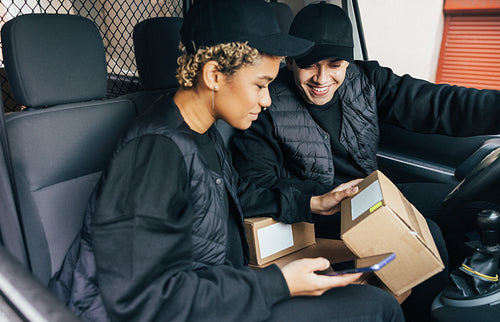 Two couriers sitting in van checking information on box for deli