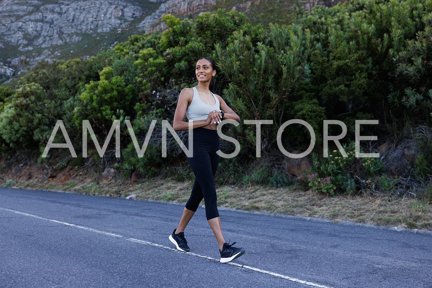 Full length of smiling sportswoman walking on an abandoned road and checking smartwatches. Cheerful female walking and looking away. 