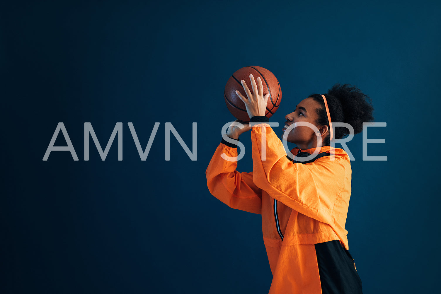 Basketball player in orange sportswear throwing a basketball over a blue background. Side view of professional basketball player practicing over blue backdrop.