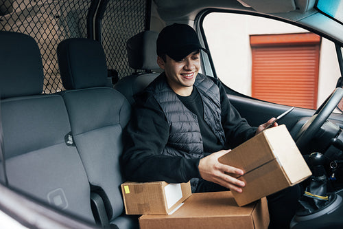 Smiling courier sitting on a driver's seat checking delivery inf