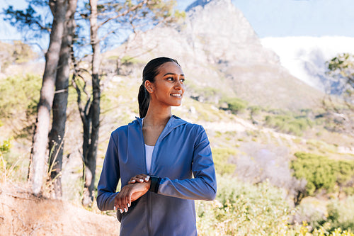 Smiling slim woman with smartwatches relaxing after training outdoors. Young female looking away during morning walk.