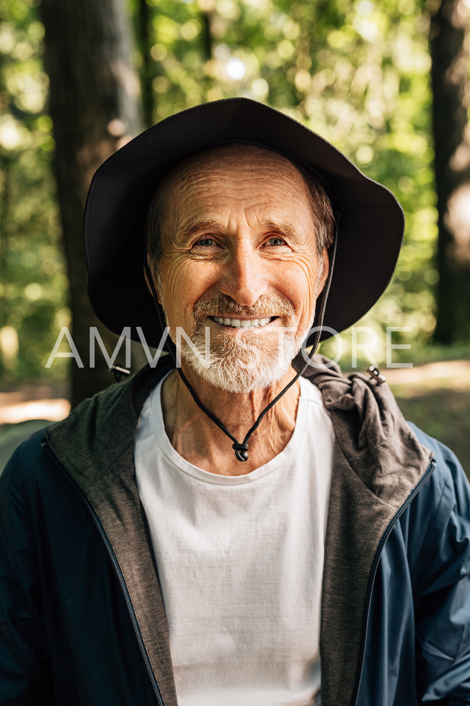 Close-up of smiling senior male wearing hat. Portrait of a cheerful mature tourist standing in a forest and looking at camera.