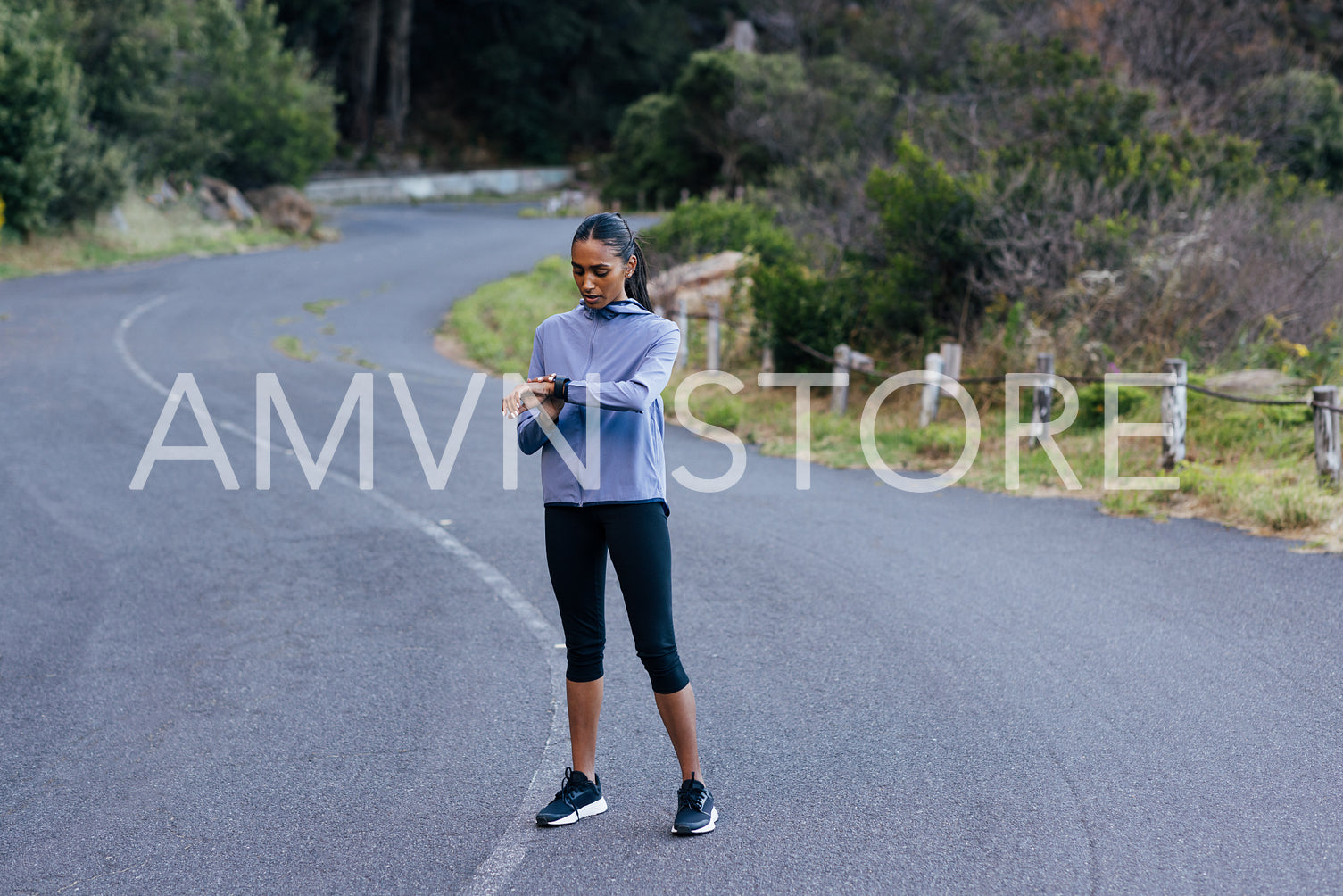 Full length of young slim female checking pulse during exercise while standing in the abandoned road. Female running taking a break checking pulse on smartwatches.